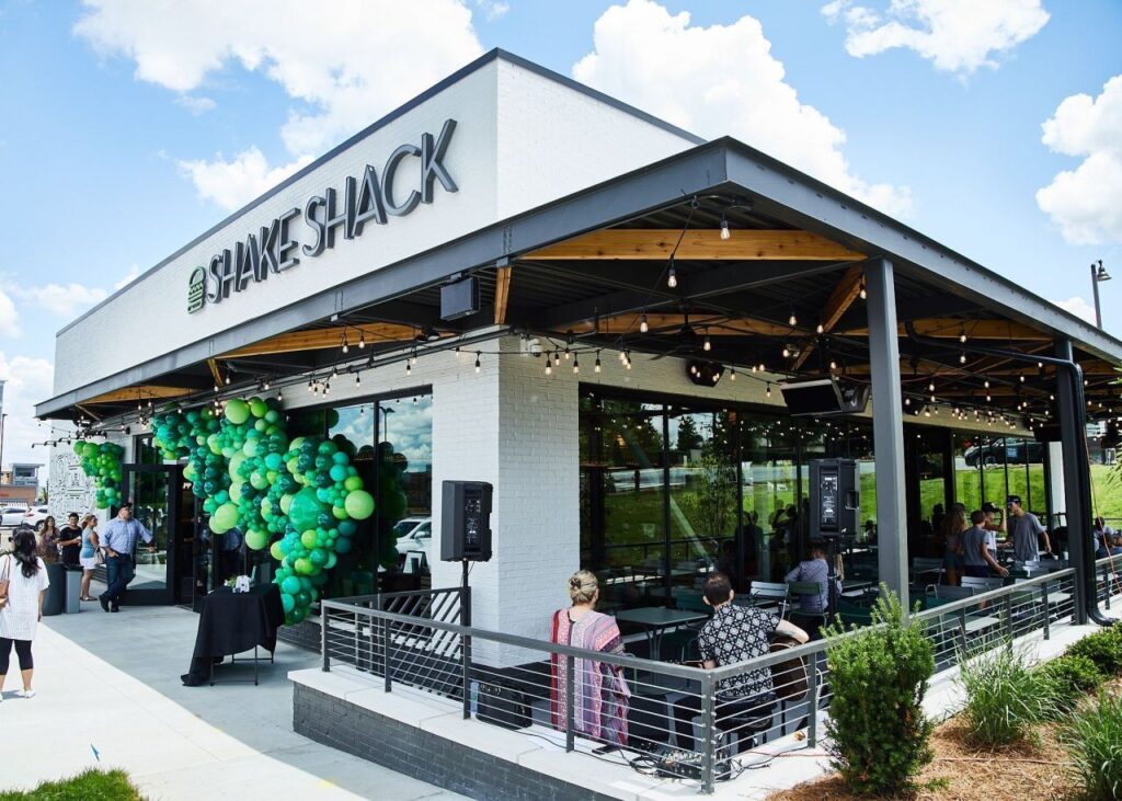 Restaurant Shake Shack animé par des clients et des centaines de ballons verts à l'avant et des chauffages au gaz.